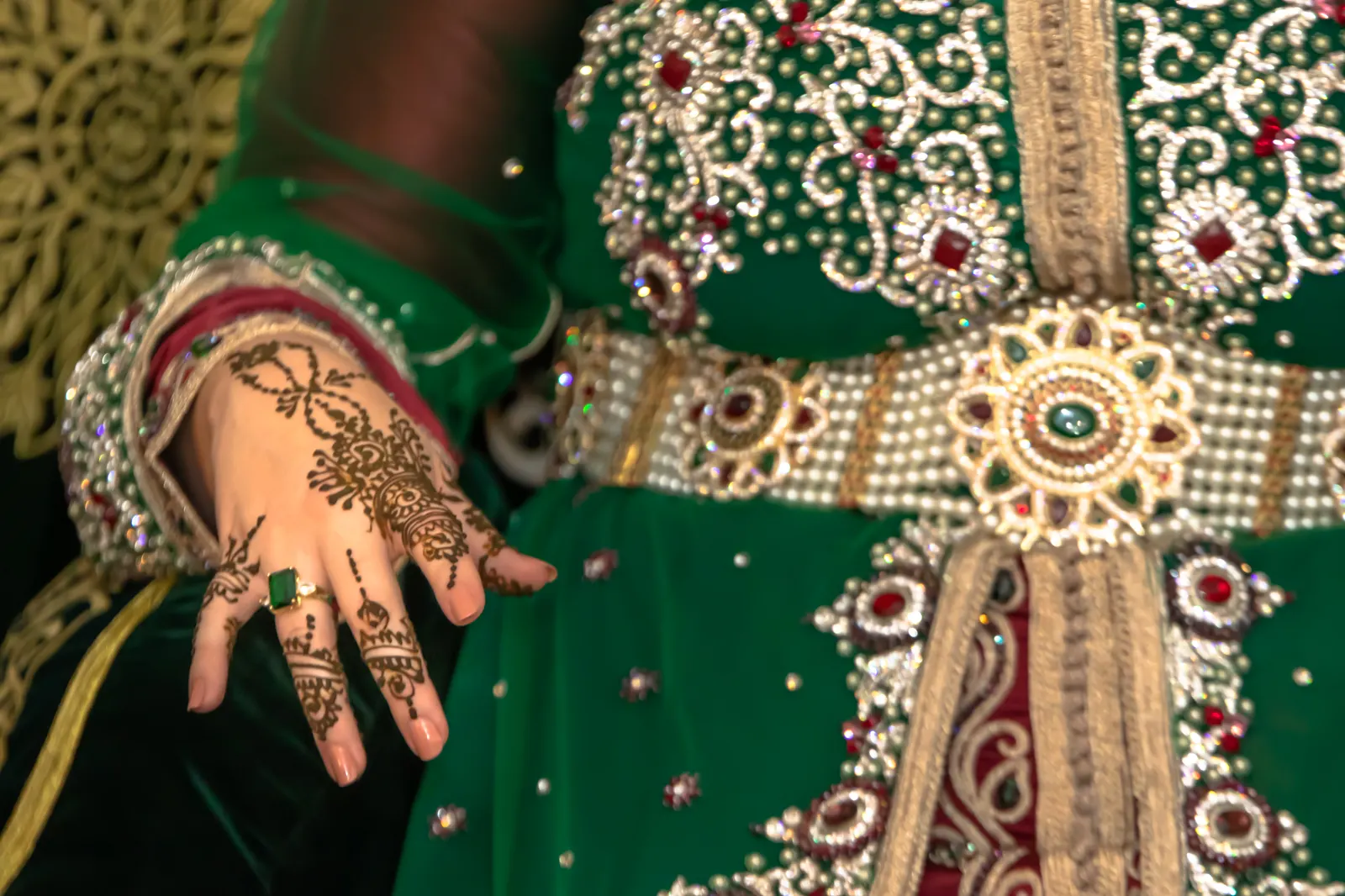 Main de mariée ornée de henné sur un caftan émeraude brodé d'or, lors d'une soirée henné marocaine